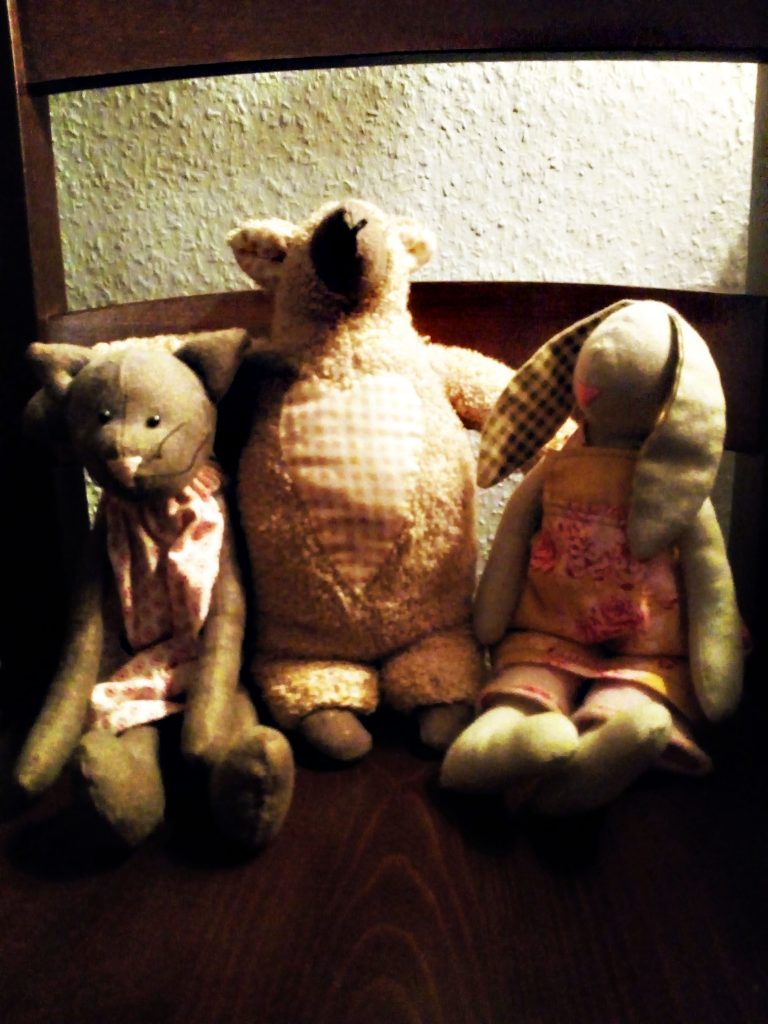 Katze, Schaf und Hase sitzen auf einem Holzstuhl nebeneinander.