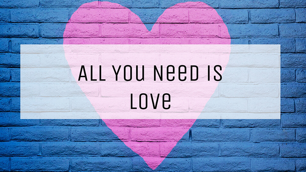 Ein rosa Herz auf einer blauen Backsteinwand. Darüber befindet sich ein weißes halb transparentes weißes Rechteck. Auf diesem befindet sich ein schwarzer Schriftzug "All you need is love" - Perfekt für die Kontakt-Seite